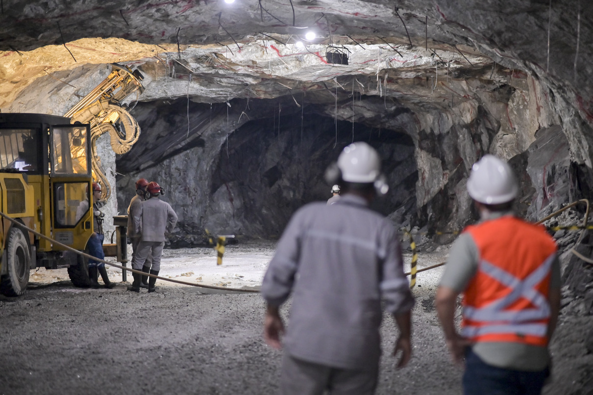 Trabalhadores atuam em galeria subterrânea de extração de lítio com equipamentos pesados.