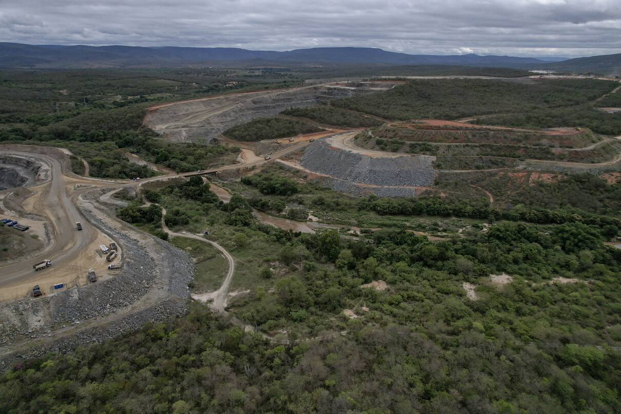 Vista panorâmica de área minerada com terraplanagem e mata ao fundo.