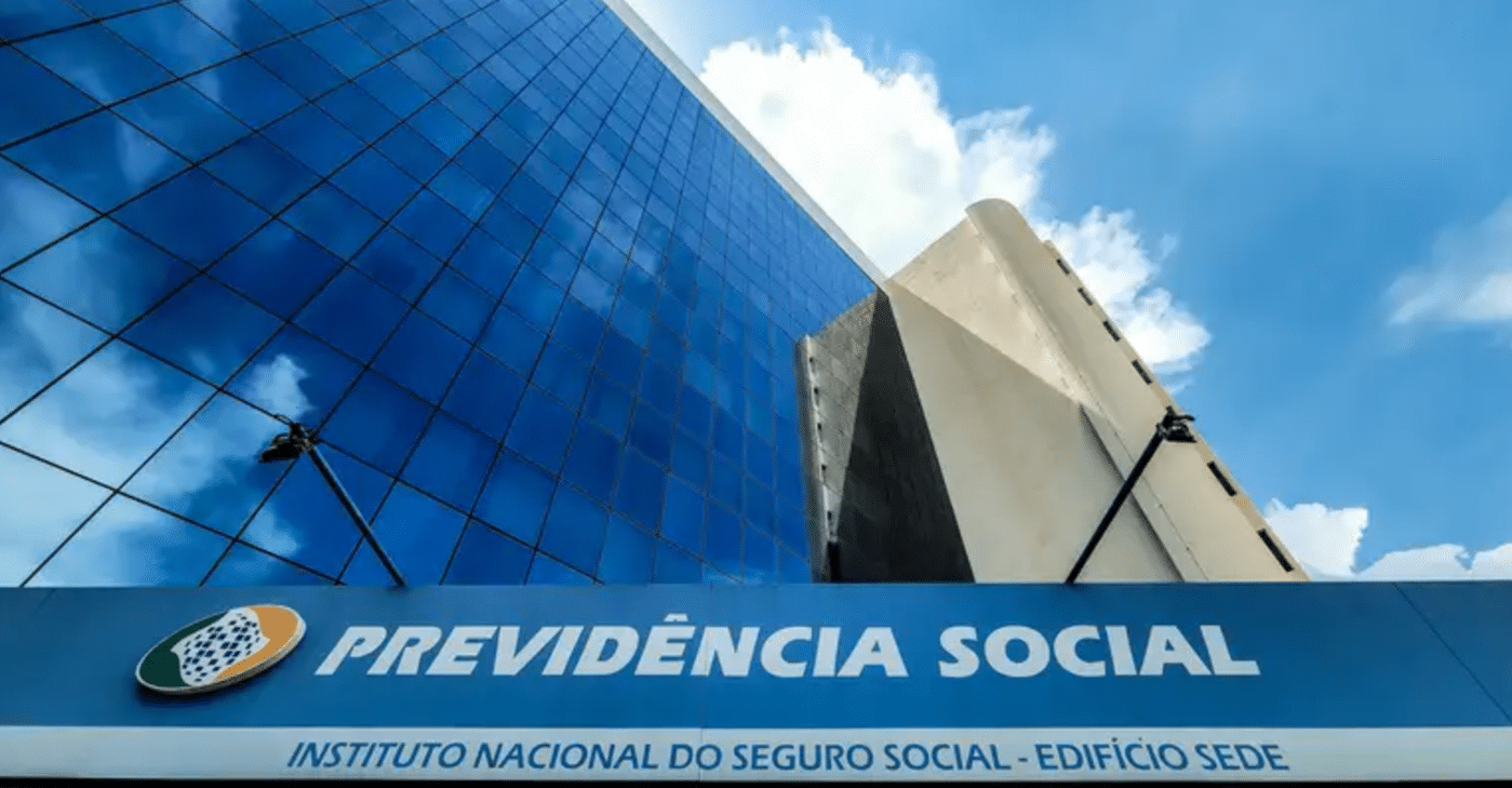 Fachada do edifício-sede da Previdência Social, com reflexo do céu nas janelas espelhadas e letreiro do INSS em destaque.