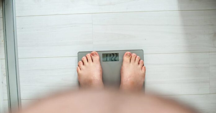 Pessoa com sobrepeso se pesando em balança digital, simbolizando controle de peso