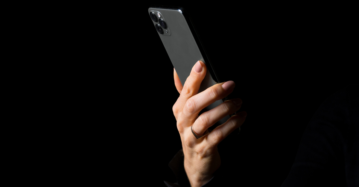 Mãos digitando em um smartphone com fundo escuro