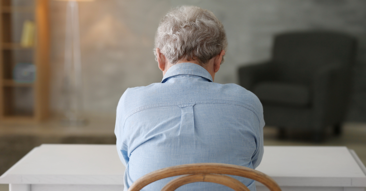  Idoso sentado sozinho de costas em ambiente doméstico, representando o impacto da solidão
