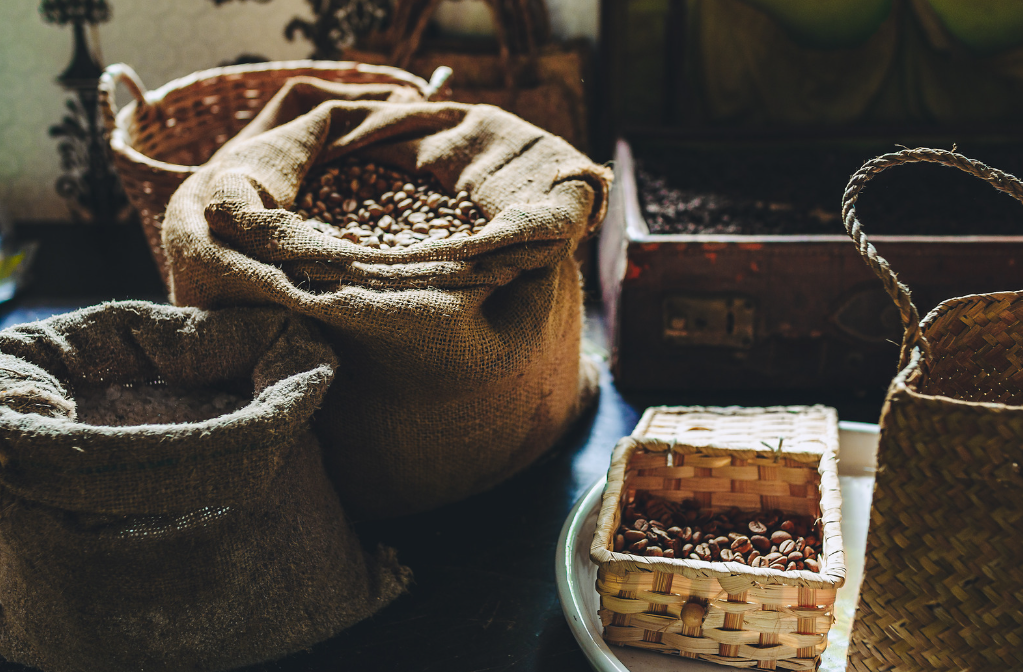 Sacas e cestos com grãos de café armazenados em ambiente rústico, iluminado naturalmente