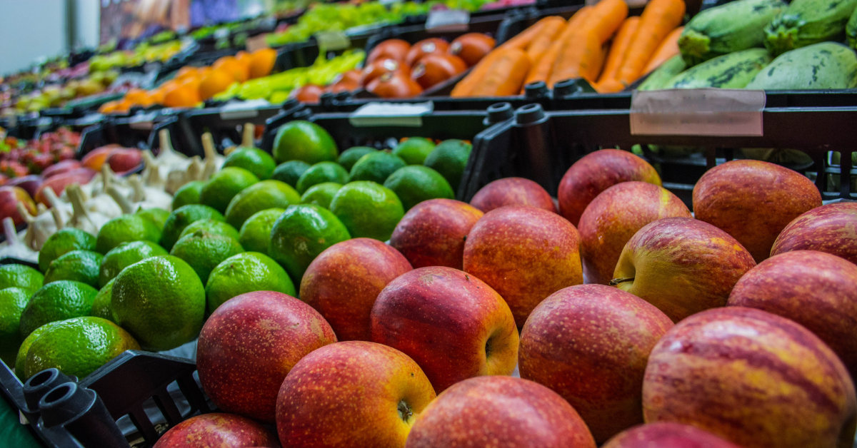 Bancas de feira com frutas e legumes frescos, como maçãs, limões, cenouras e abobrinhas