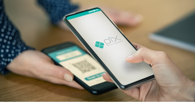 Pessoa realiza pagamento usando Pix em smartphone, aproximando o celular de outro aparelho com QR Code.