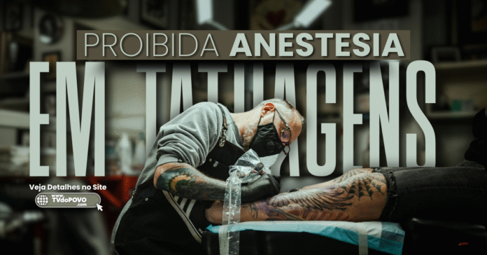 Homem tatuando perna de cliente com tarja informativa sobre a proibição de anestesia em tatuagens, conforme resolução do CFM