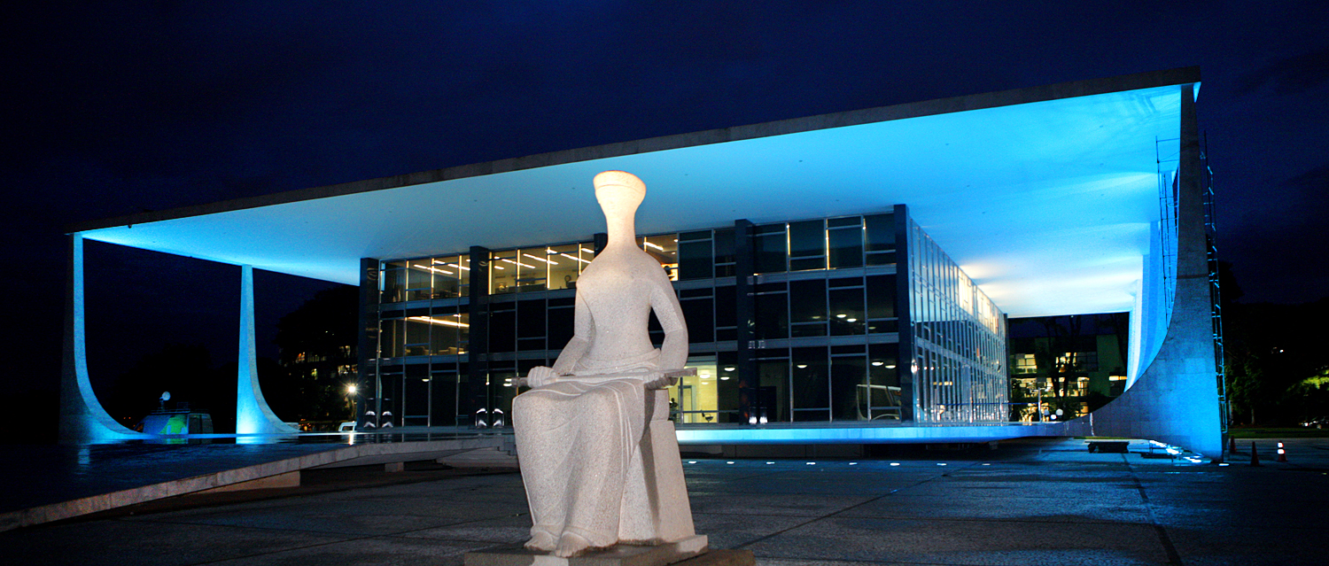 Fachada iluminada do Supremo Tribunal Federal à noite, com escultura da Justiça em destaque.