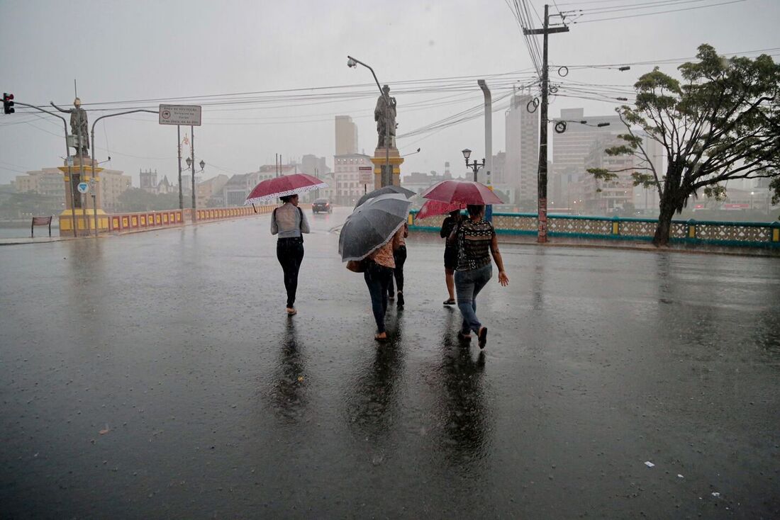 Pessoas atravessam ponte com guarda-chuvas durante chuva forte em Recife