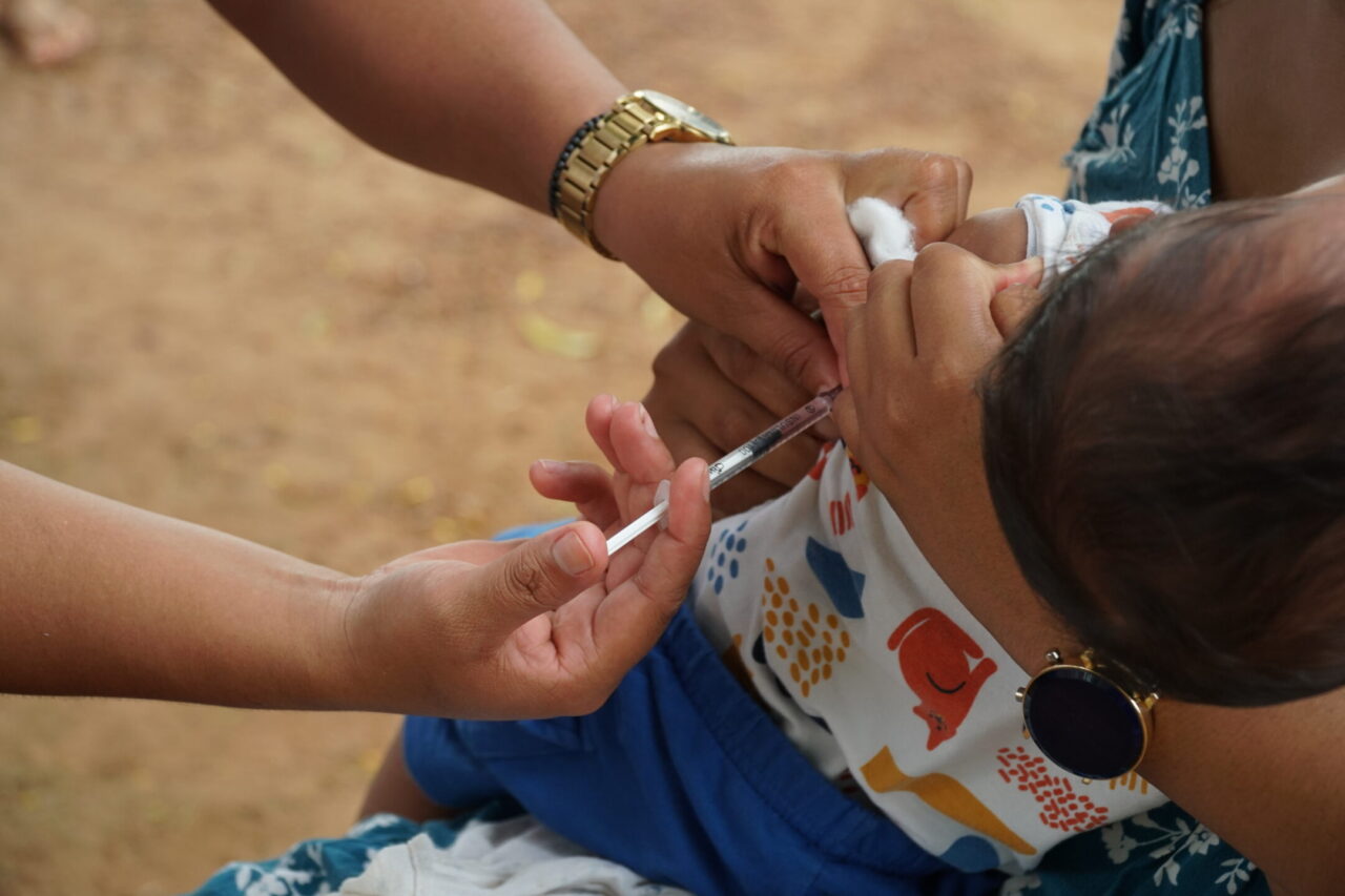 Profissional de saúde aplica vacina em bebê nos braços da mãe durante ação pública de imunização infantil em Rondônia