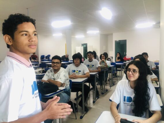 Estudantes do Idep participam de aula em Porto Velho, com jovem apresentando atividade oral enquanto colegas acompanham atentamente em sala de aula.