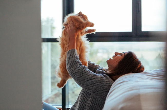 Pessoa sorrindo enquanto brinca com seu gato em casa, simbolizando amor e cuidado no Dia Internacional do Gato.
