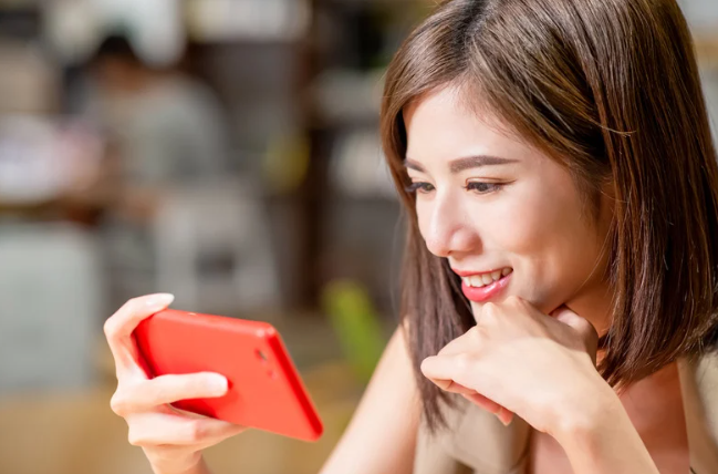 Jovem assiste a vídeos no celular com atenção e sorriso, ilustrando o hábito de ver conteúdos em velocidade acelerada.