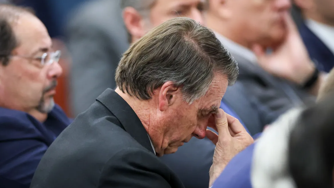 Jair Bolsonaro com expressão de preocupação durante sessão, levando a mão ao rosto.