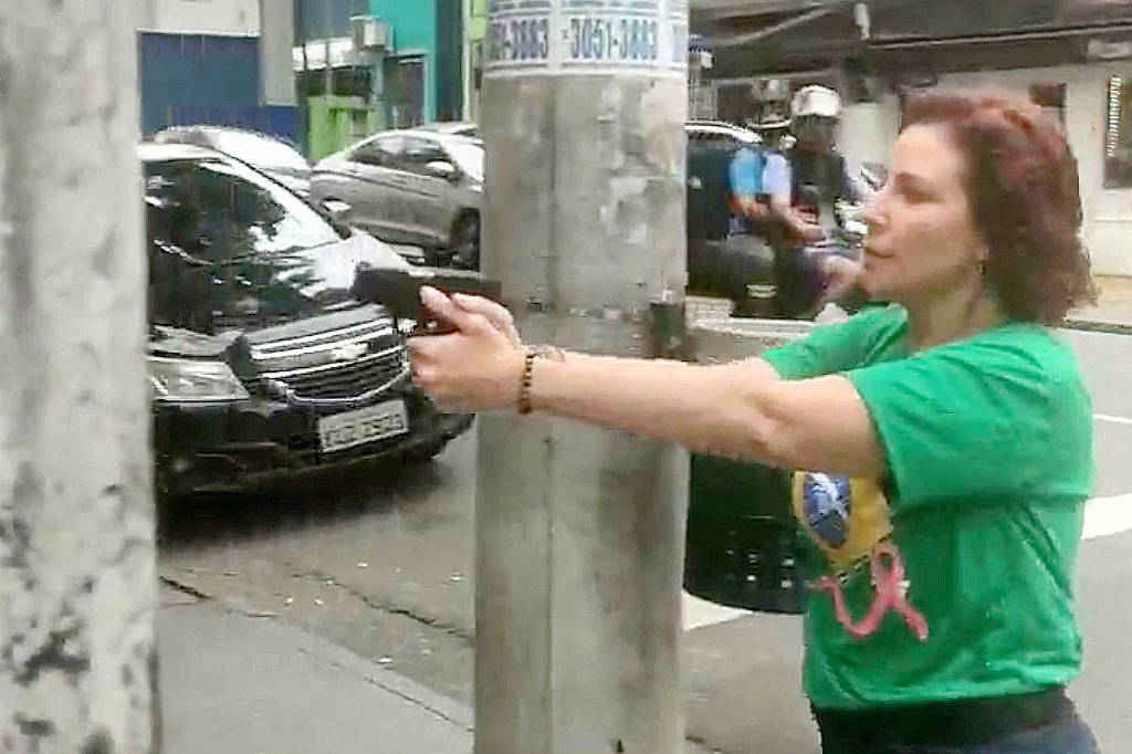 Carla Zambelli com camiseta verde aponta arma em via pública durante perseguição em São Paulo.
