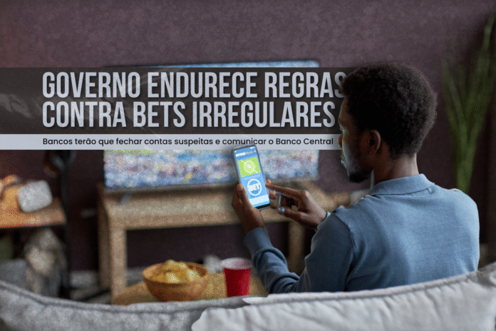 Homem segura celular com aplicativo de apostas esportivas enquanto assiste jogo de futebol na TV, representando o endurecimento das regras contra bets irregulares.