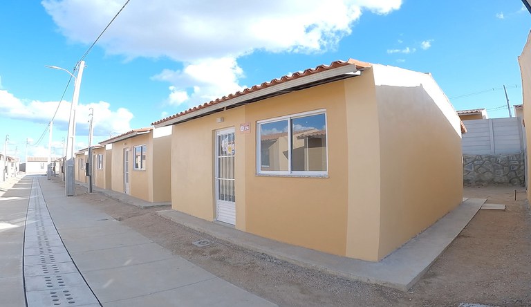Imagem mostra fileira de casas populares recém-construídas pelo programa Minha Casa Minha Vida, com paredes claras e céu azul.